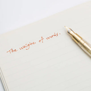 Gold brass dip pen writing over notebook page with colorful cursive ink lines