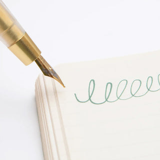 Close-up gold brass dip pen nib applying ink onto paper with teal writing