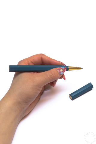 Hand holding dark teal rollerball pen with gold tip and star-pattern cap