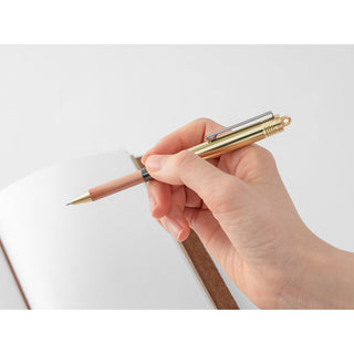 Hand holding a brass ballpoint pen with copper barrel and metal tip exposed