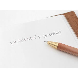 Brass ballpoint pen writing beside a notebook page with printed text