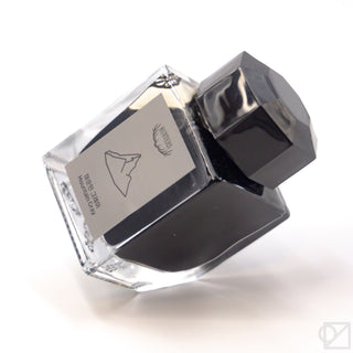Square ink bottle with black cap and off-white label, shown open and tilted