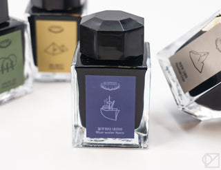 Close-up ink bottle with black cap and blue-water navy label on the front