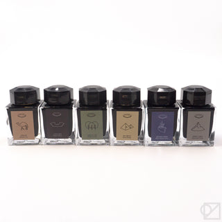 Row of six square ink bottles with black faceted caps and color-coded labels