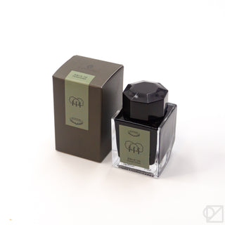 Ink bottle with dark body, black faceted cap, and pale green label on the glass