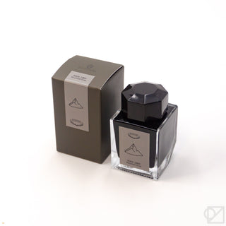 Ink bottle with dark glass, black faceted cap, and light label with tree icon