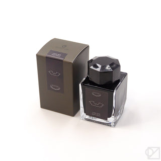 Ink bottle with dark glass, black faceted cap, and purple label with mountain icon