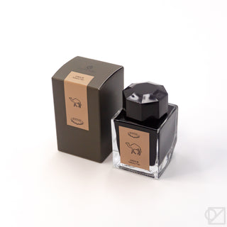 Ink bottle with dark glass, black faceted cap, and tan label with horse icon