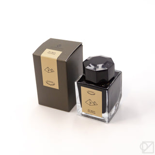 Ink bottle with dark glass, black faceted cap, and tan label with scale icon