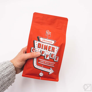 Red coffee bag held in hand with Diner Coffee label and 12oz badge.