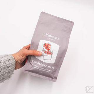Herman's Moyamensing Blend 12oz coffee pouch held in hand, light brown/red logo