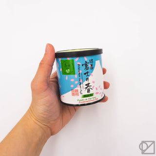 Ceremonial matcha tin held in a hand, black lid and blue label