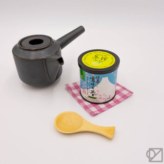 Ceremonial matcha tin with black teapot and wooden scoop, plus yellow matcha powder