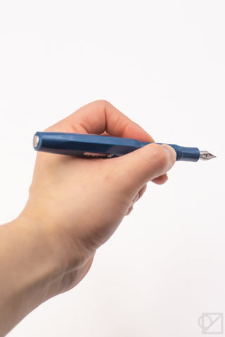 Teal fountain pen held in hand with pointed nib visible