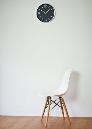 Round black wall clock with white hands and numerals on light wall