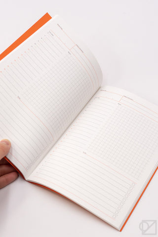 A5 daily planner open to a grid page with an orange binding edge and a hand holding it.