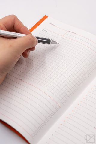 A5 spreadsheet notebook with white pages, orange bookmark tab, and pen-ready grid lines