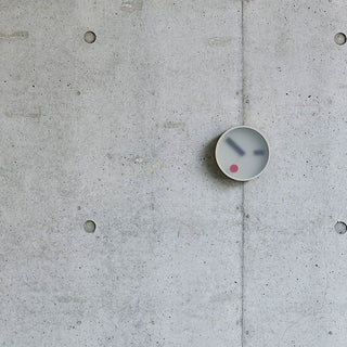 Round wall clock mounted on concrete wall, light grey bezel and red center dot