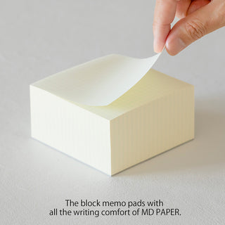 Cream sticky note block; a finger lifts the top sheet from the grid stack.