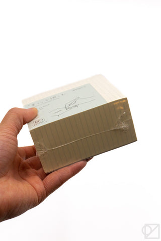 Hand holding the memo pad block, showing grid paper and back cover label.