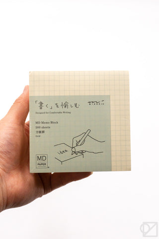 Hand holding a grid memo pad block with blue MD PAPER label.