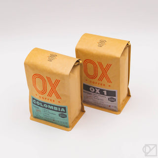Two whole bean coffee blend bags: OX 1 and COMBIA on kraft packaging