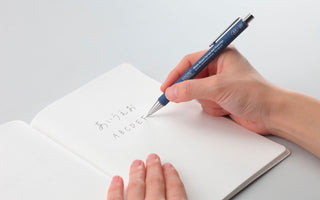 STÁLOGY 028 0.5mm gel ink rollerball pen in blue, held over an open notebook