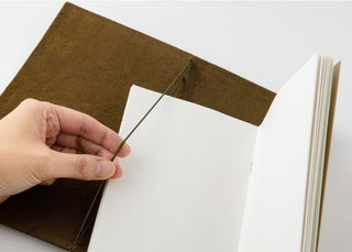 Hand inserting paper into olive notebook with tied cord and open pages
