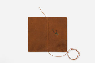 Brown notebook cover open with repair strings laid out on white background