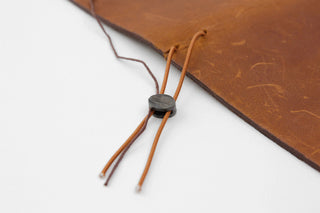 Brown notebook corner with tied repair cords and a small bundled stitch piece