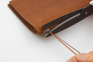 Brown notebook corner with repair tool and orange cord held by a hand