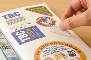 Sticker release paper with TRAVELER'S coffee and label stickers, hand peeling
