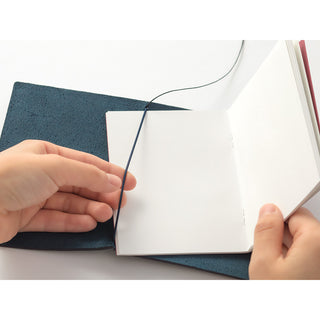 Blue passport-size notebook cover with pages being inserted, elastic strap visible
