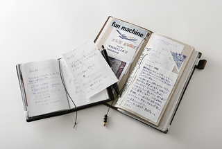Black passport-size travel notebook open with handwritten pages and card inserts