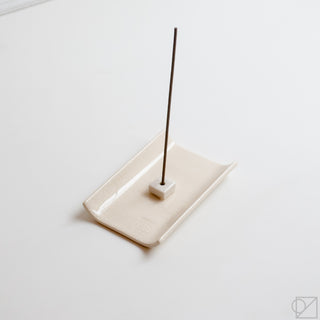 White tray incense burner with central stick stand and dark incense stick