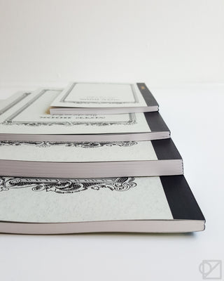 Cream notebook stack with ornate frame cover detail, angled side view