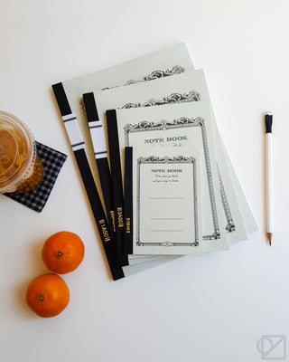 Stack of cream notebooks with ornate border cover design and black spines