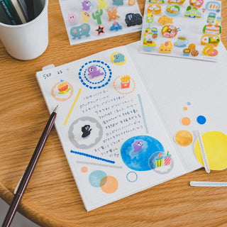 Open illustrated journal with colorful stickers, pen and paint palette