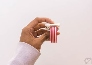 Hand holding KOKUYO Karu-Cut clip dispensing red-and-white striped tape