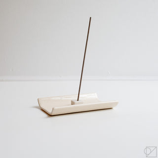White plate incense burner with raised stick holder and dark incense stick