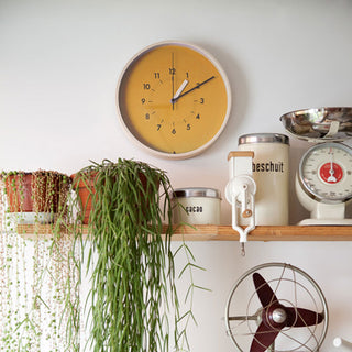 Round wall clock with orange-yellow dial and black hour and minute hands.