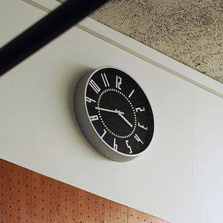 Wall-mounted black clock with silver rim, white hour markers and minute dial