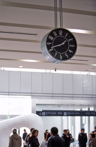 Large black wall clock with silver rim, white numerals and hands mounted indoors