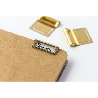 Brass index clip holding brown paper, with 'Summer' label and hinged frame
