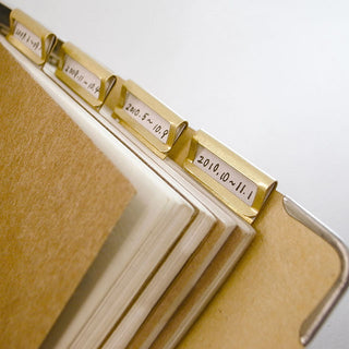 Gold-toned brass index clips with stamped labels, close-up on a notebook edge