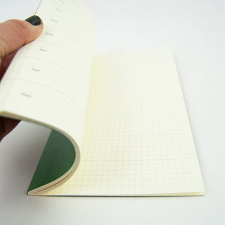 Open notebook pages with light grid paper; held at the spine by a hand