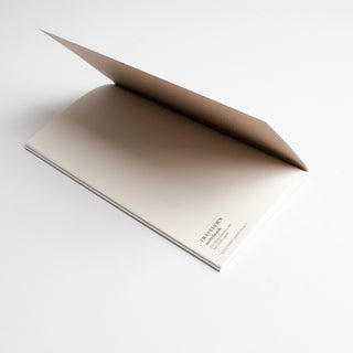 Kraft grid notebook lying flat with visible spine edge and minimal cover print
