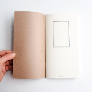 Blank notebook open, showing brown back cover and a framed insert on the page