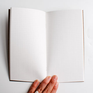 Grid notebook with two open pages, white paper, and brown spine