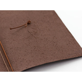 Brown leather notebook cover corner with tied strings and button detail.